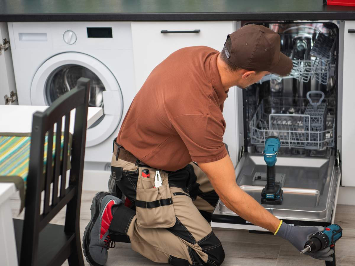 Technician repairing a dishwasher in a residential kitchen